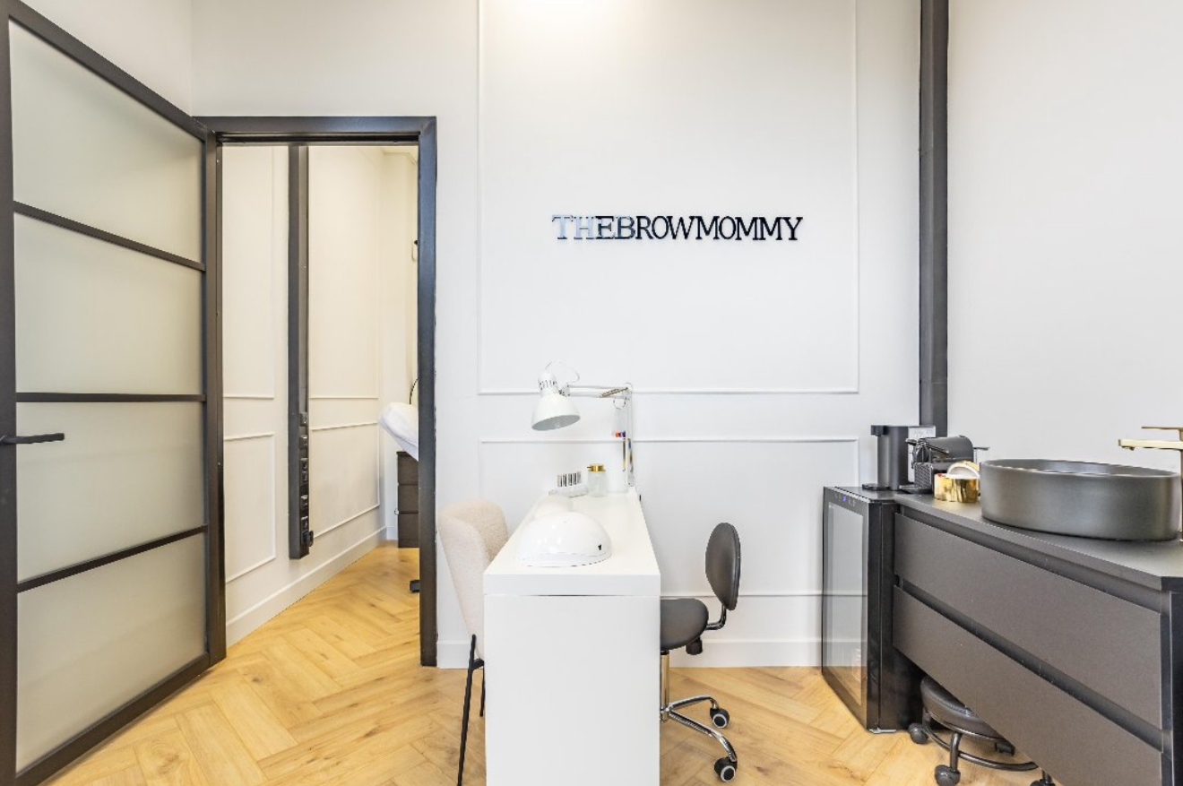 Behandelplek bij Thebrowmommy: witte tafel, grijze waskom, visgraatvloer en de naam op de muur