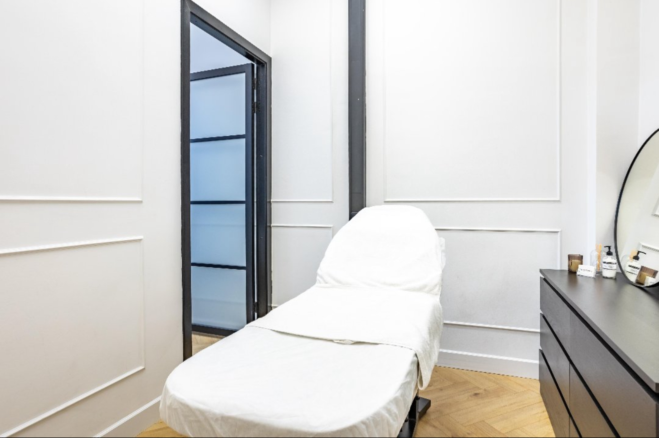 Behandelkamer met een wit bed en een zwarte stalen glazen deur