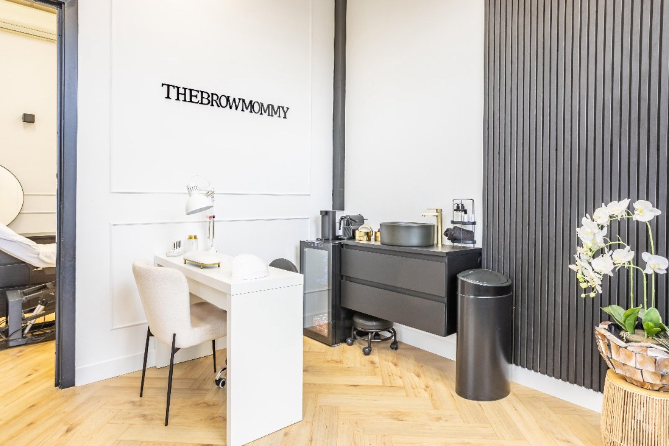 De salon van Thebrowmommy met de naam op de muur, een witte tafel en een zwarte lattenwand